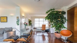 Un salon moderne avec un plancher en bois, un canapé gris, un fauteuil en cuir noir, une grande plante verte et un meuble en bois.