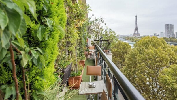 Un balcon offrant une vue sur la Tour Eiffel, entouré d’une végétation luxuriante et agrémenté de plantes en pot.