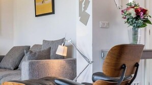 Un salon moderne avec un fauteuil de relaxation en bois, un canapé gris et une lampe sur pied.