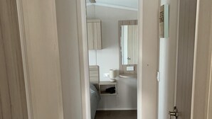 A narrow hallway leading to a bedroom with a bed, bedside table, and a mirror. - Hot tub Break Away Castle View (Lincoln)