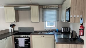 A compact kitchen with a gas stove, oven, and sink, wooden cabinets, and a sign above the window. - Hot tub Break Away Castle View (Lincoln)