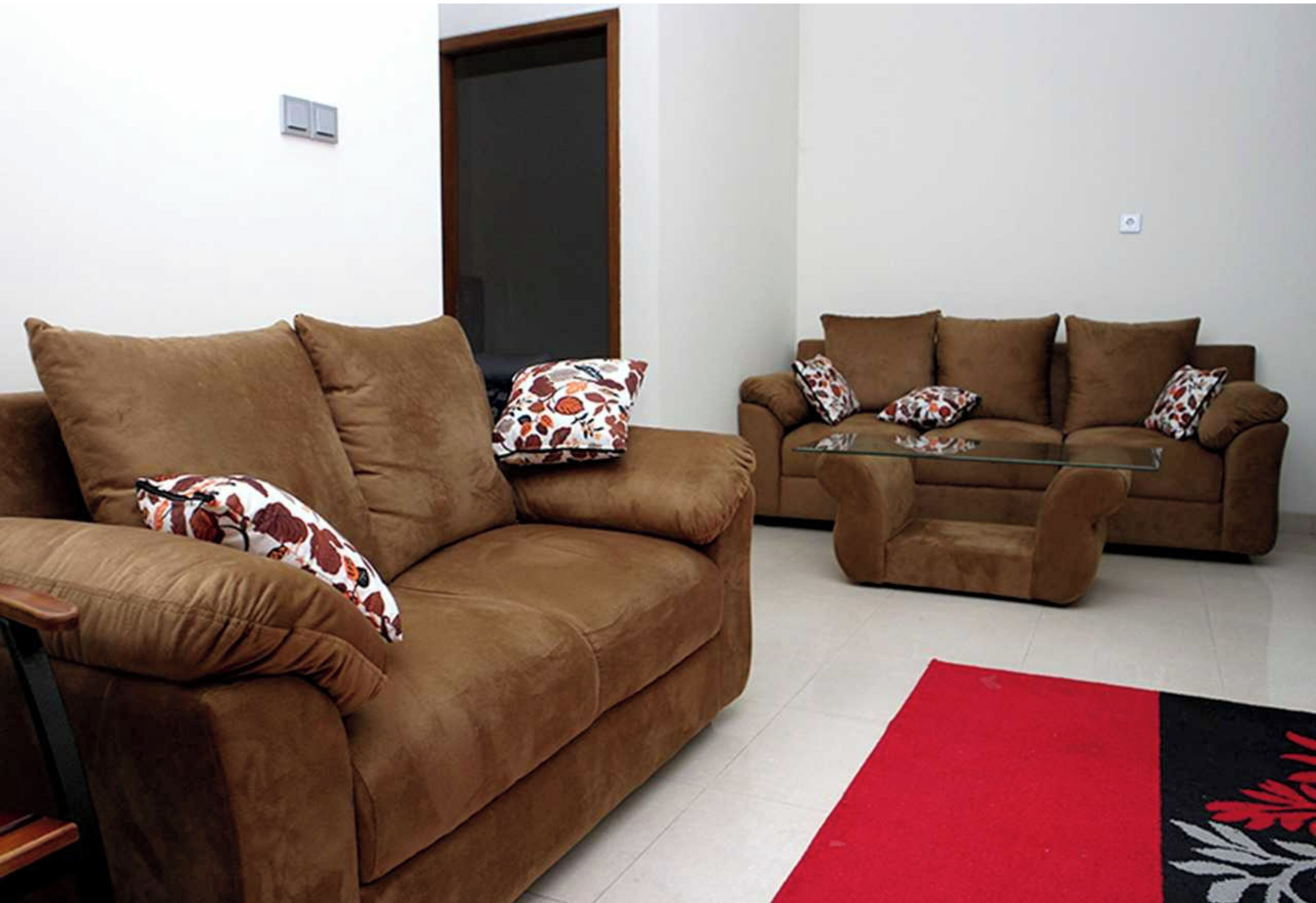 A living room with two brown sofas, a glass coffee table, and a red rug.