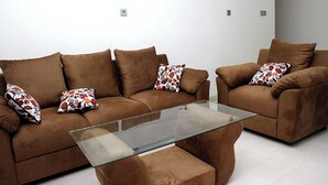 Una sala de estar con dos sofás marrones, una mesa de centro de vidrio y almohadones estampados.
