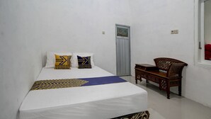 A single-bed room with a white bedspread, two pillows with geometric patterns, a wooden bench, and a door with a small window. - Hotel O Alif House Syariah 2 (Kediri)