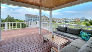 A covered outdoor deck with a wooden ceiling, a white railing, and a sofa with cushions. - Oceanview Hawks Landing in Oak Island: 3BR, 2BA retreat for 6 guests. (Oak Island)