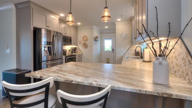 A kitchen with a marble countertop, stainless steel appliances, pendant lighting, and a herringbone-patterned backsplash. - Oceanview Hawks Landing in Oak Island: 3BR, 2BA retreat for 6 guests. (Oak Island)