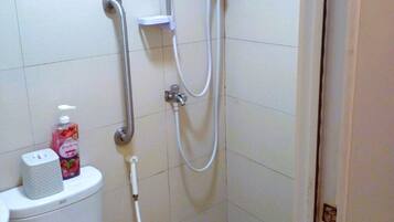 Une petite salle de bain carrelée, équipée de toilettes, d’une douche et d’un sèche-mains.