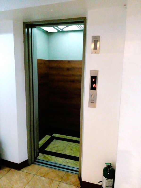 An elevator with a digital display, a fire extinguisher, and a tiled floor.