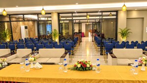A conference room with rows of blue chairs, a long table with yellow tablecloth, water bottles, and floral centerpieces. - Hotel Fountain (Dhaka)