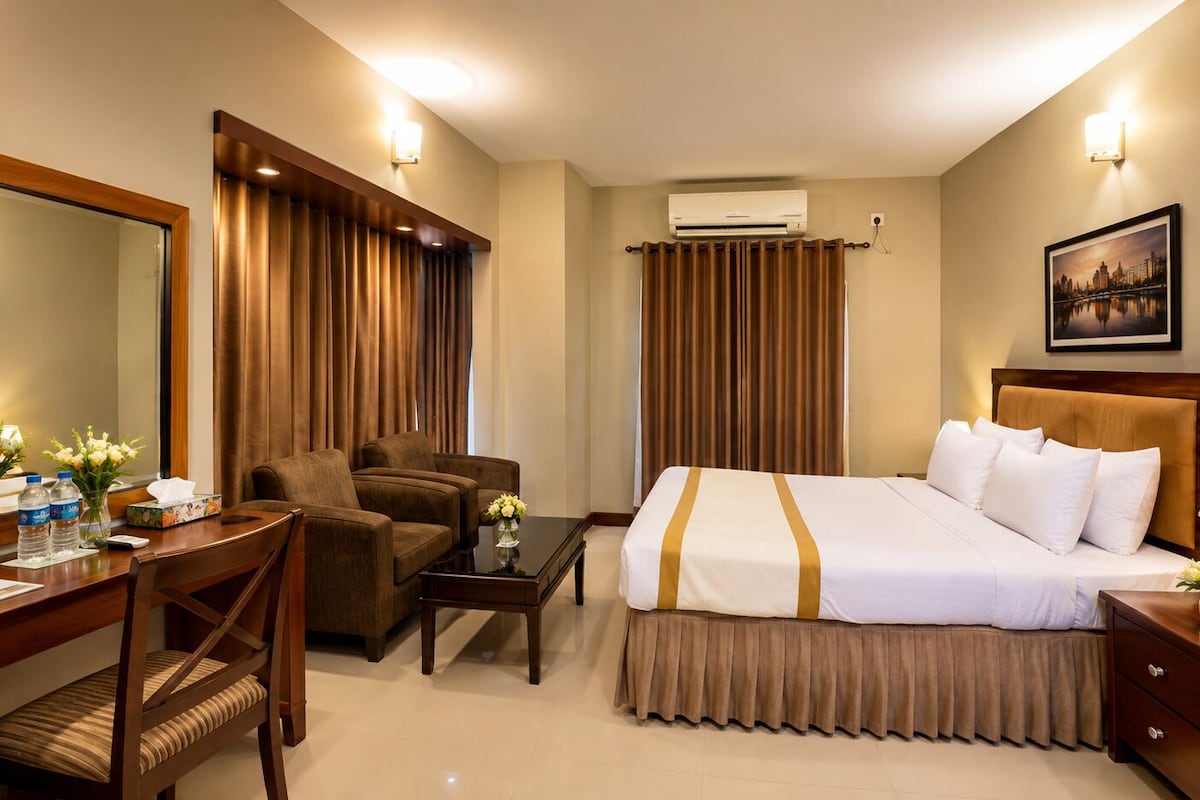 A hotel room with a bed, a desk, a chair, a table, and a nightstand.