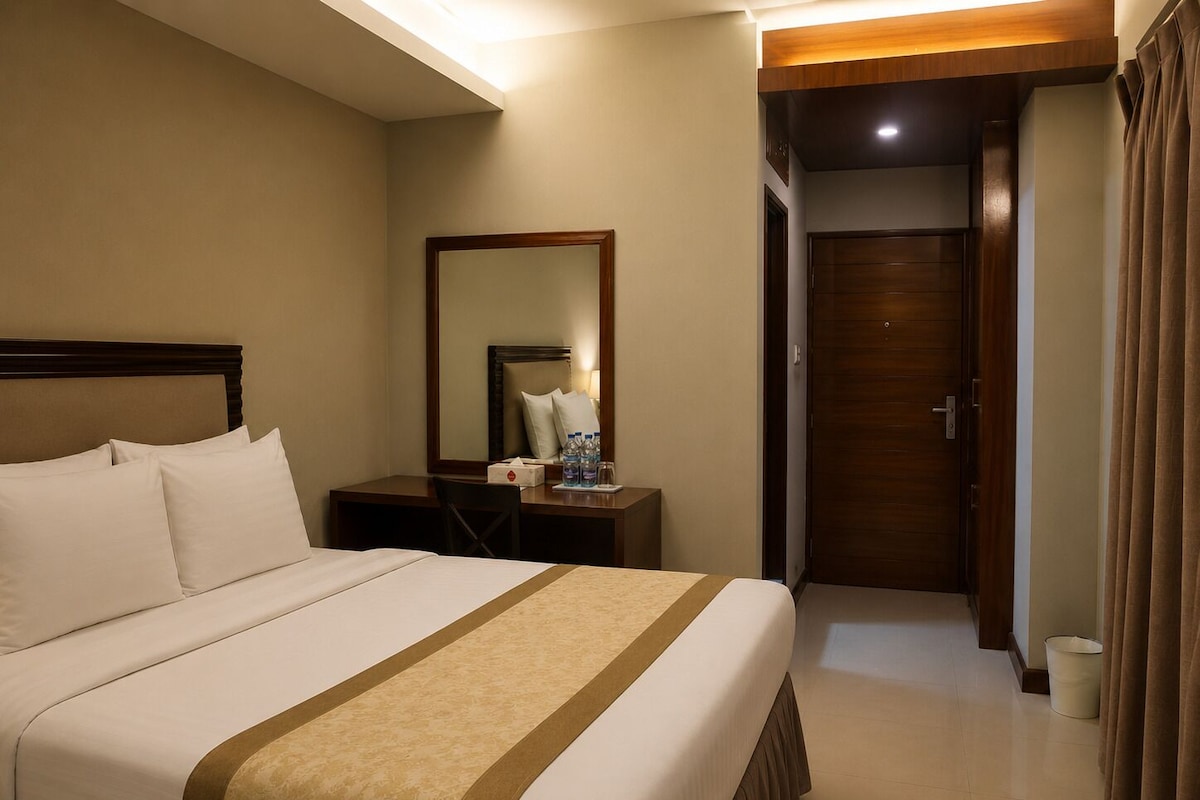 A hotel room with a large bed, a bedside table with a lamp, a mirror, and a door leading to another room.