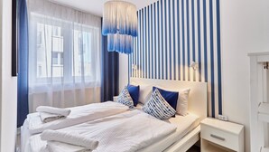 A modern bedroom with a large bed, white bedding, and blue and white striped wall panels. - Apartamenty Sun&Snow Bałtyk (Swinoujscie)