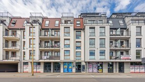 A row of modern multi-story residential buildings with balconies, a visible storefront, and a clear sky. - Apartamenty Sun&Snow Bałtyk (Swinoujscie)