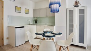 A modern kitchen with white cabinets, a dining table set for four, and a ship model on the wall. - Apartamenty Sun&Snow Bałtyk (Swinoujscie)