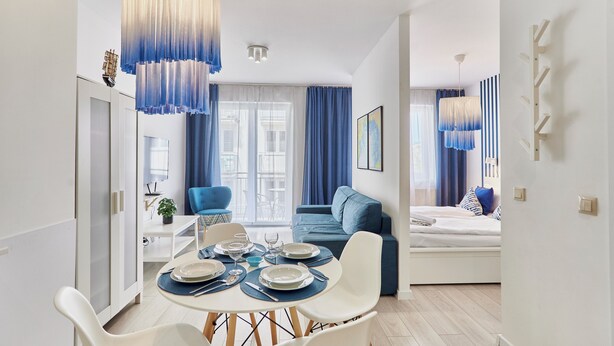 A modern living room with a sofa, dining table set for two, and a TV mounted on the wall. - Apartamenty Sun&Snow Bałtyk (Swinoujscie)