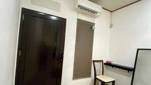 Una habitación con una puerta de madera oscura, una ventana con persianas, una silla y un estante pequeño.