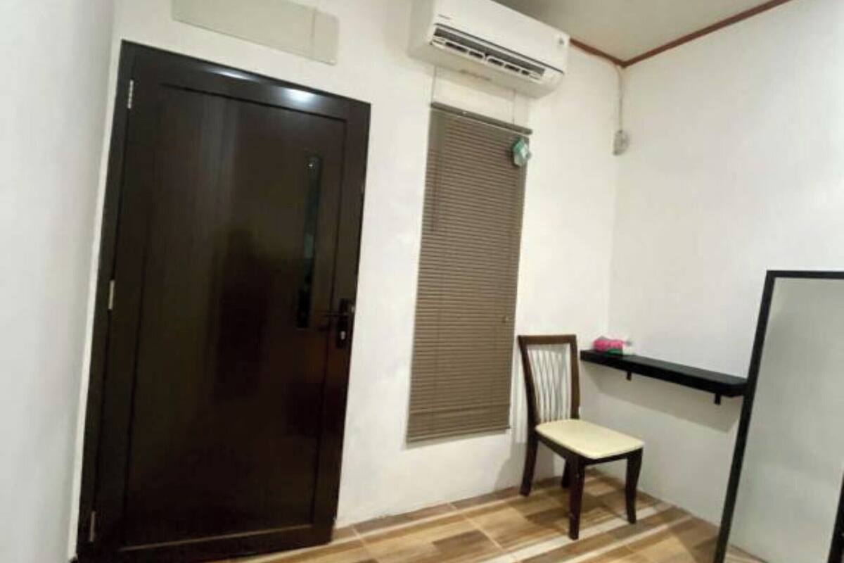 Een kamer met een donker houten deur, een raam met zonwering, een stoel en een klein plankje.