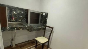 Una habitación pequeña y compacta con suelo de madera, una sola silla, encimera de mármol con lavabo e iluminación en el techo.