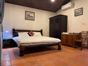 A bedroom with a wooden bed, a nightstand, a desk with a lamp, a wardrobe, and a chair.