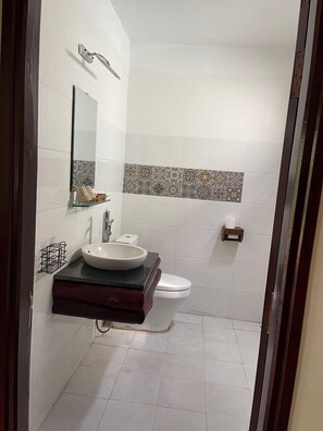 A bathroom with a white sink, a mirror, a toilet, and a shower area.