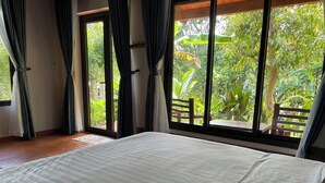 Ein Schlafzimmer mit einem großen Bett, einer Schiebetür zum Balkon mit Blick auf Grünflächen.