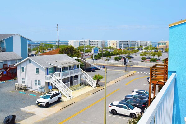 A coastal hotel with a white exterior, a balcony, and a parking lot with several cars.