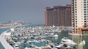 Un port de plaisance où sont amarrés de nombreux bateaux, un grand bâtiment d’hôtel en arrière-plan et une vue dégagée sur la mer.