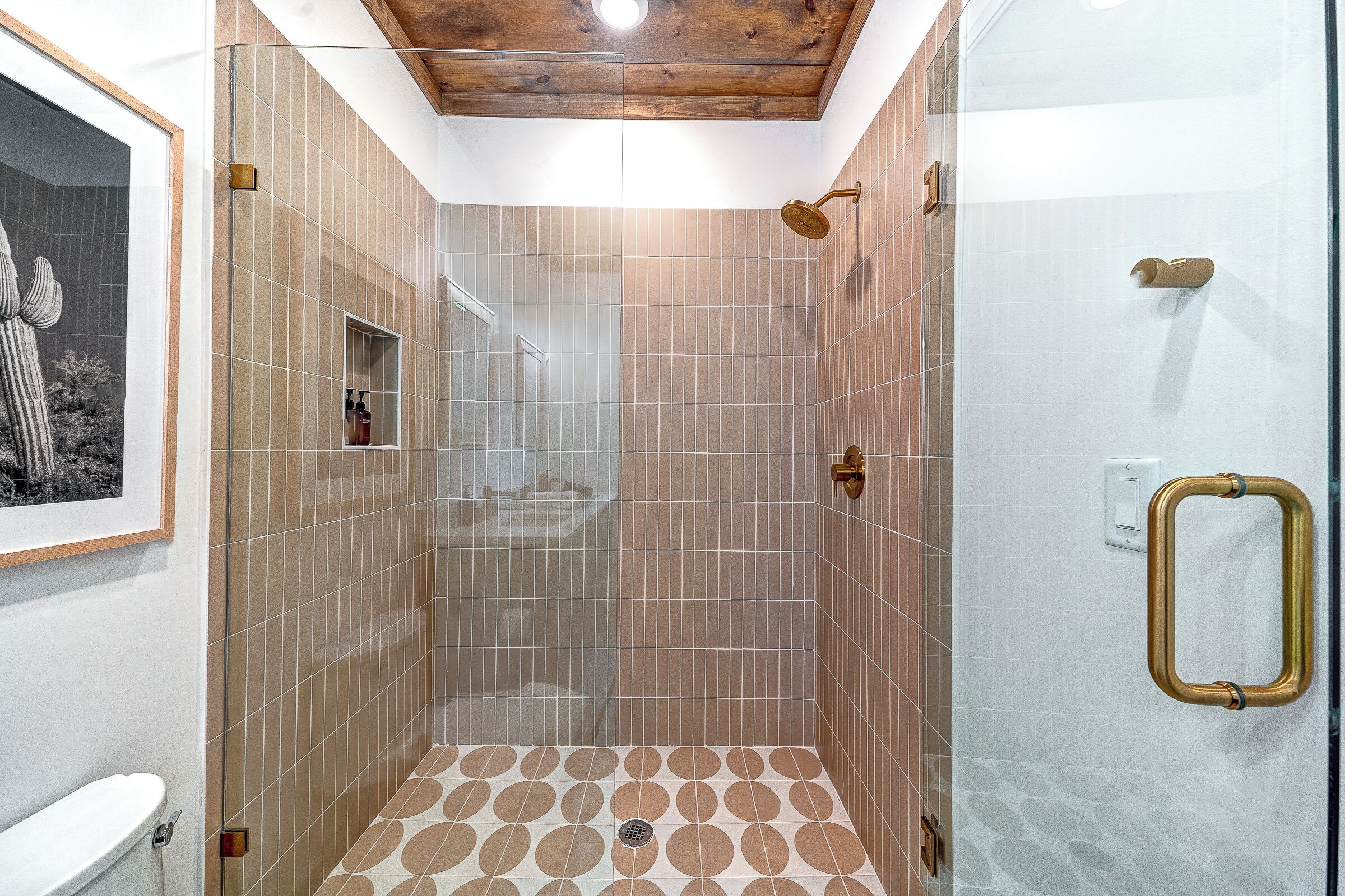 A shower area with a glass door, beige patterned tiles, and a wooden ceiling.