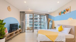 Habitación de hotel con cama, televisor, planta, ventana con vistas a edificios y un cuadro en la pared.