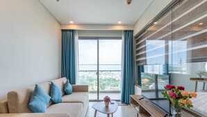 Una sala moderna con un sofá, una mesa de centro, un televisor y un balcón con cortinas.