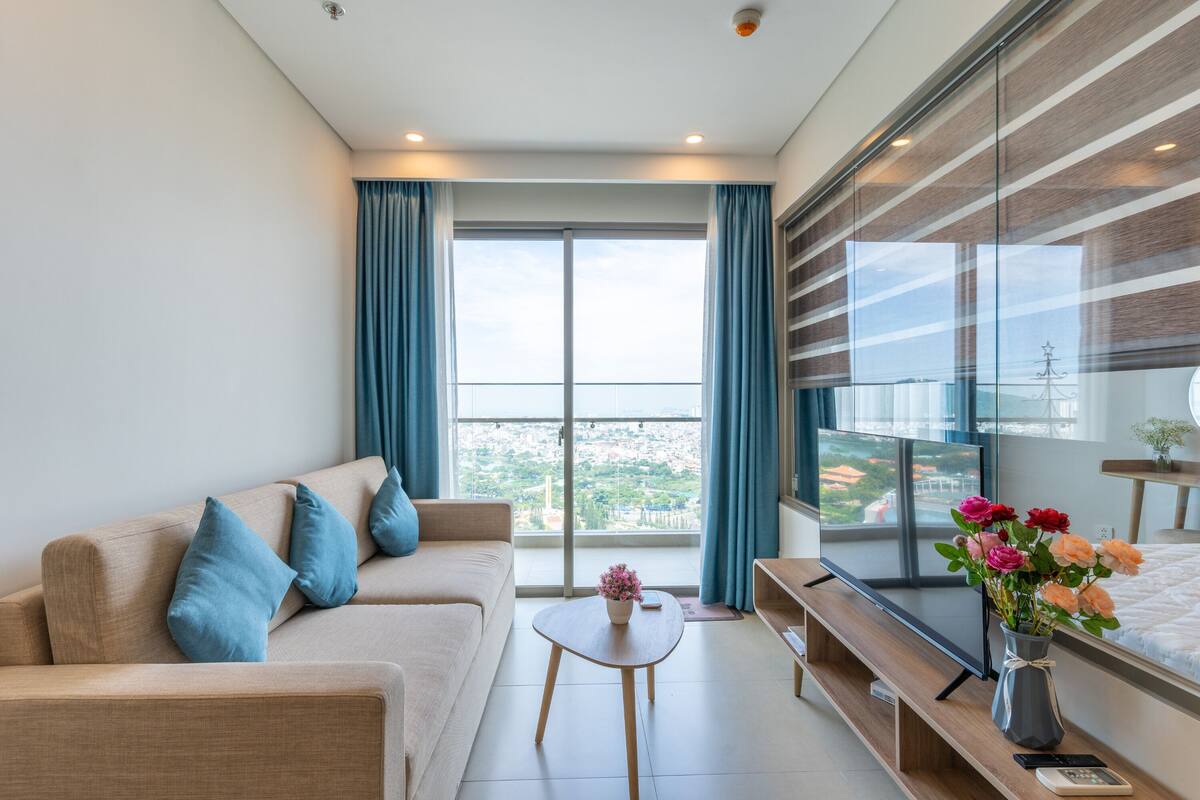 A modern living room with a sofa, a coffee table, a TV, and a balcony with curtains.