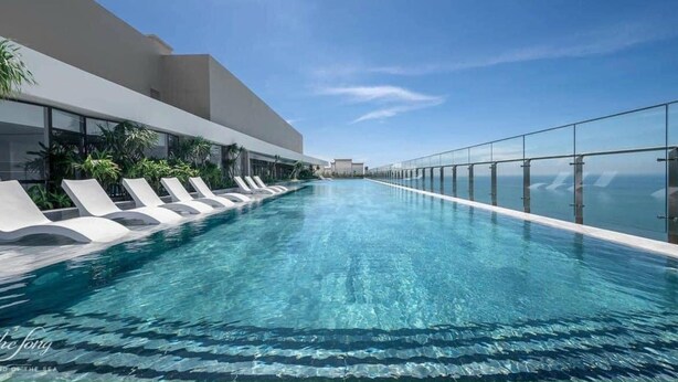 Una piscina infinita moderna con agua azul cristalina, rodeada de sillas de descanso y una barandilla de vidrio.