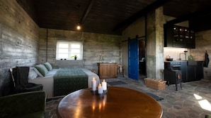 A rustic room with a bed, a wooden table with candles, a window, and a kitchenette. - Jakob's old Farmhouse (Rangárþing eystra)