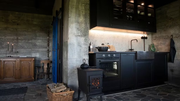 A rustic kitchen with a wood-burning stove, a built-in oven, and a stone floor. - Jakob's old Farmhouse (Rangárþing eystra)