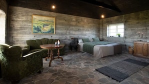 A rustic room with a stone floor, a green sofa, a round wooden table with candles, a bed with a green blanket, and a painting on the wall. - Jakob's old Farmhouse (Rangárþing eystra)