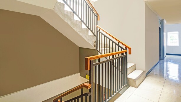 A staircase with wooden handrails and metal railings, leading to a landing with a light-colored floor.