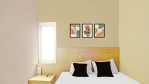 A hotel room with a bed, a nightstand, a window, and three framed artworks on the wall.