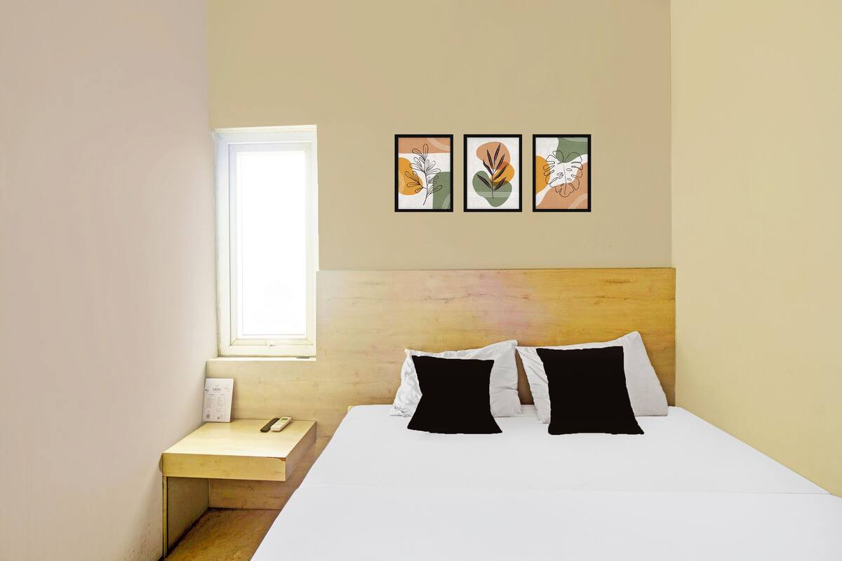 Habitació d'hotel amb un llit, una vetustat, una finestra i tres quadres emmarcats a la paret.