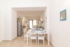 A dining area with a white table and chairs, a refrigerator, and a vase with flowers. - Appartamento Mirto In The City Center (Santa Teresa di Gallura)