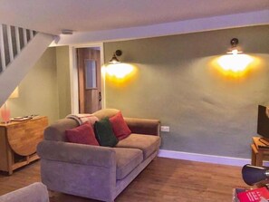 Relax in this inviting living room with a comfortable sofa, wooden side table, and desk, surrounded by a warm ambiance.