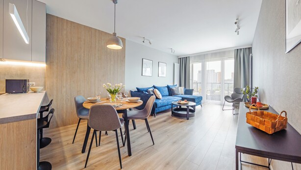 A modern living room with a dining area, a blue sofa, and a kitchen area with a microwave. - Apartamenty Sun&Snow Baltea (Gdansk)
