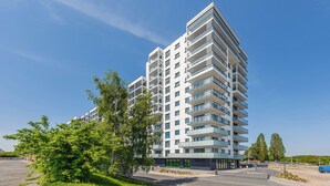 A modern multi-story building with balconies, a parking area, and greenery. - Apartamenty Sun&Snow Baltea (Gdansk)