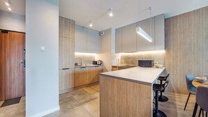 A modern kitchen with wooden cabinetry, a central island, and a dining area with a bar stool. - Apartamenty Sun&Snow Baltea (Gdansk)