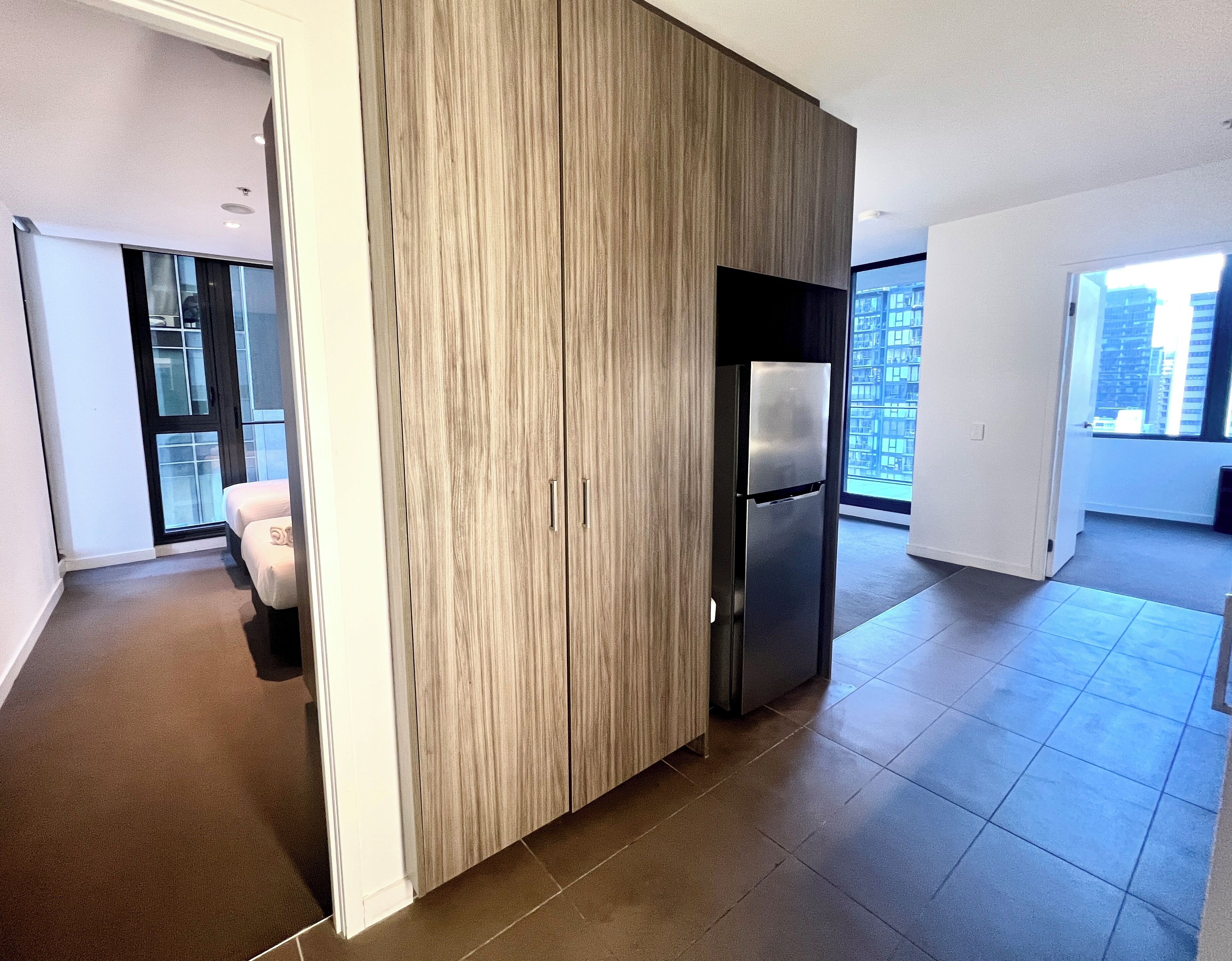 Een modern appartement met een groot raam, een ingebouwde houten scheiding en een roestvrijstalen koelkast.