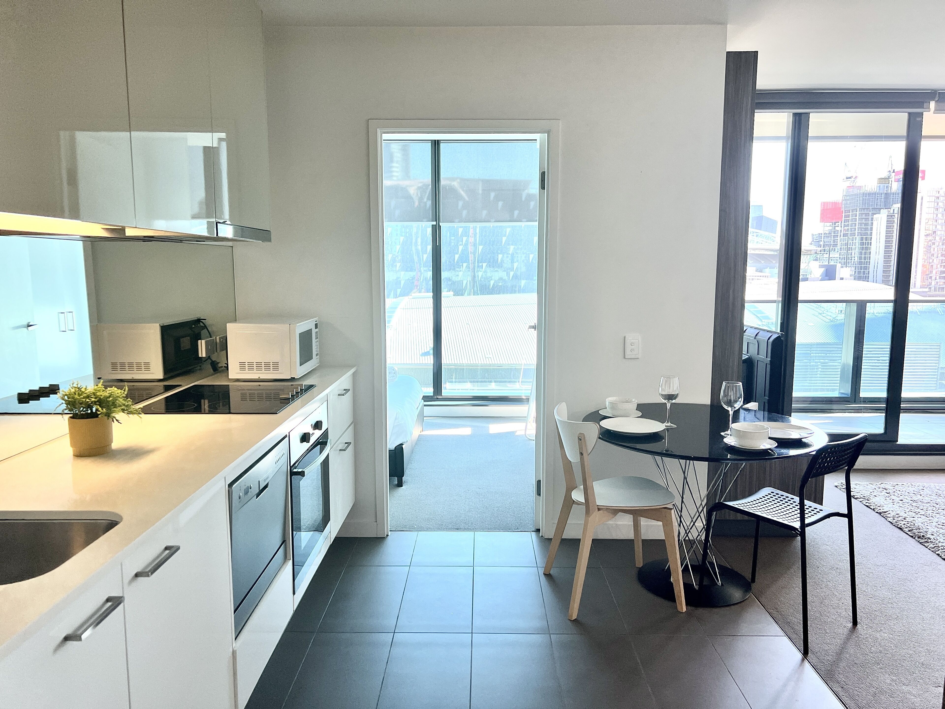 A modern kitchen with white cabinets, a microwave, and a stove. There is a dining area with a table, chairs, and a view of the city through large windows.