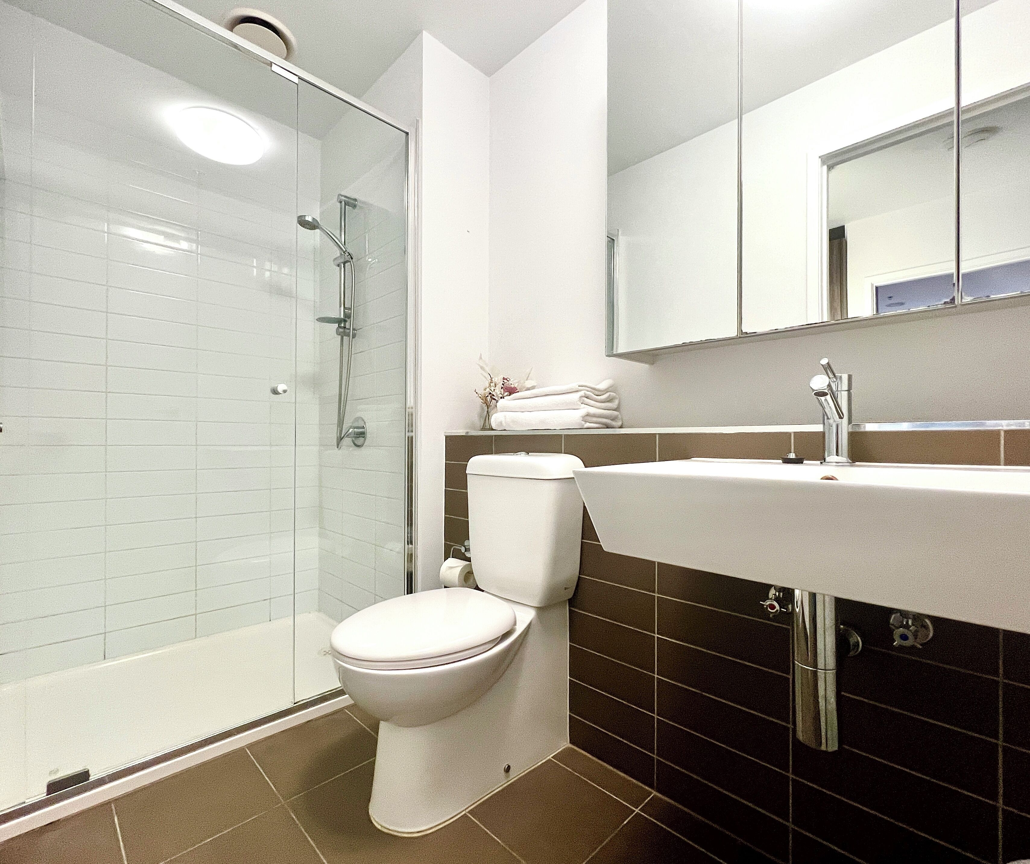 Un baño moderno con ducha de vidrio, inodoro blanco y lavamanos con espejo.