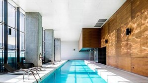 Une piscine intérieure à l’eau d’un bleu limpide, entourée de murs carrelés et d’un mur en lambris de bois d’un côté.