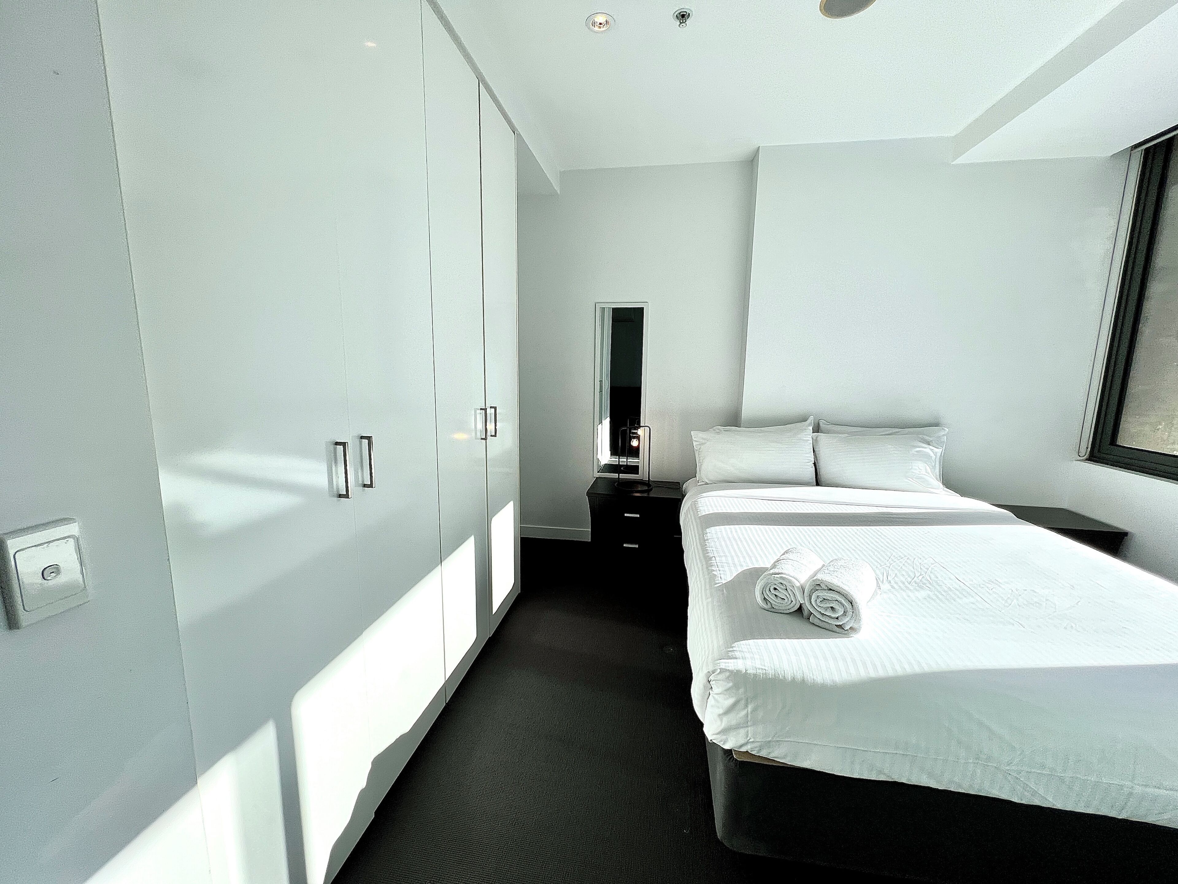Ein modernes Hotelzimmer mit einem großen Bett, einem Kleiderschrank, einem Nachttisch und einem Spiegel.