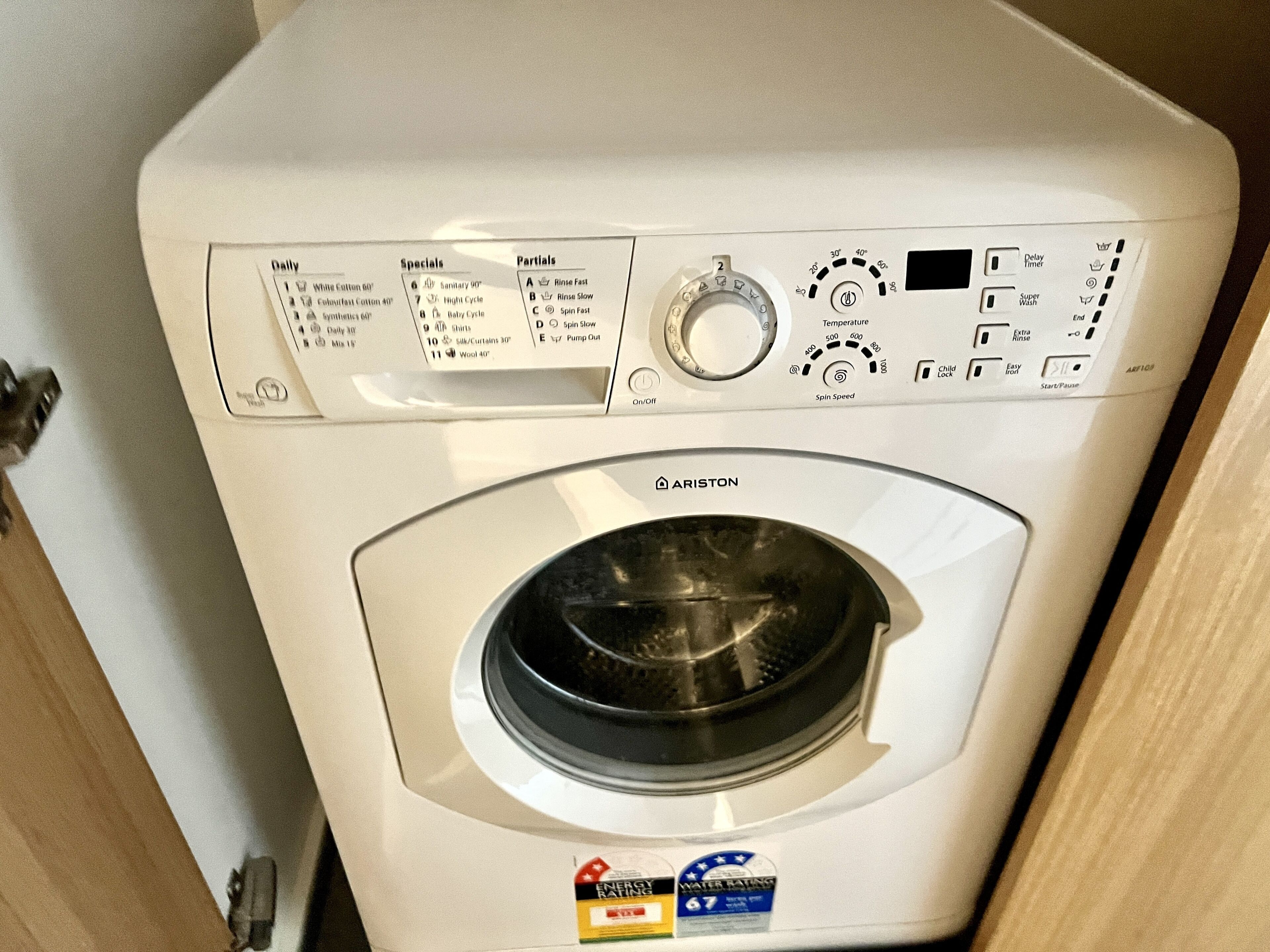 A front view of a white washing machine with a control panel, including a dial for temperature and spin speed, and a label indicating energy and water efficiency ratings.