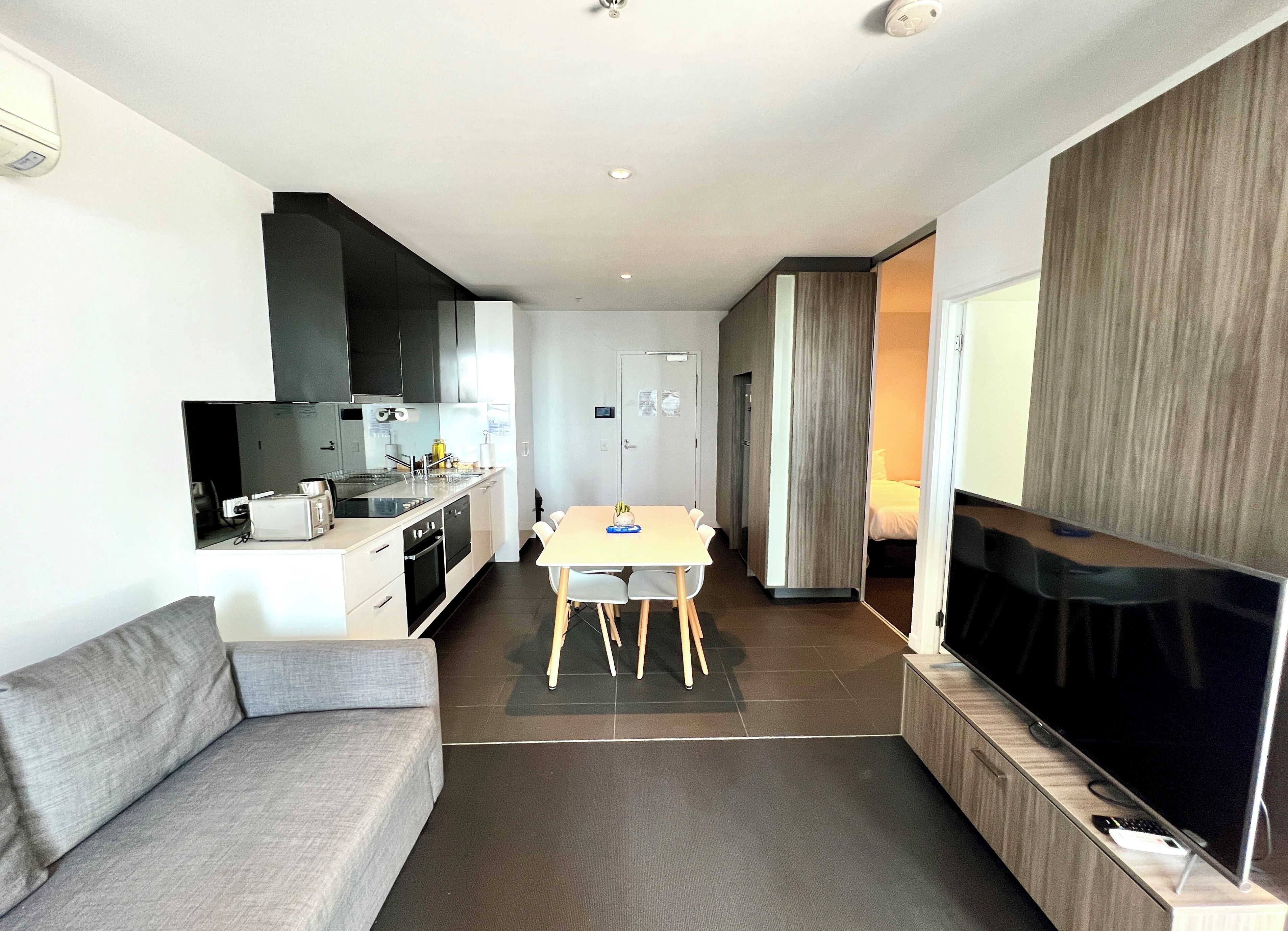 Een ruimtelijke leefruimte met een kitchenette, een eethoek, een bank en een televisie.